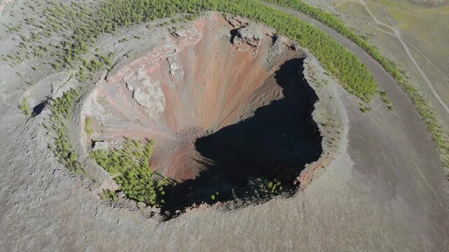 Aerial view of volcanic crater mountain showing eroded caldera slopes and barren rocky terrain. Overhead perspective reveals dramatic geology, crater walls, ash layers, and natural landforms.