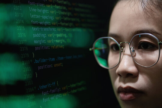 Young woman focused on code display. Background code flows in green against dark screen