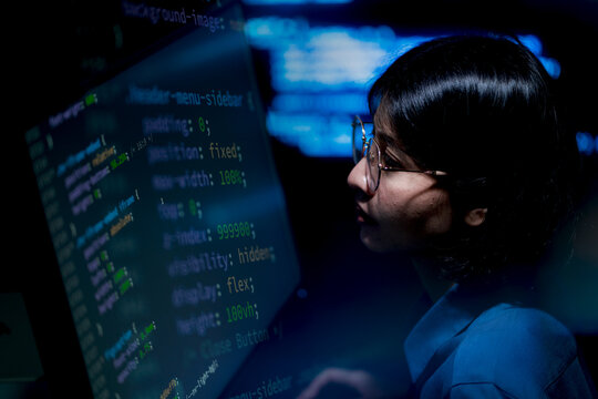 Focused programmer studies glowing code on large screen. Perfect for tech, development, or innovation themes