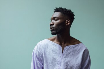 Obraz premium Male african adult threequarter portrait wearing loose white shirt on muted green background with contemplative pose