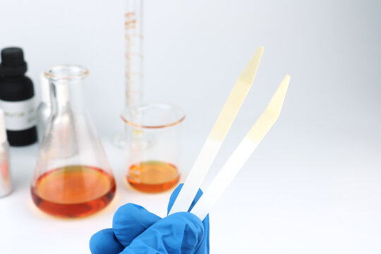 blotter papers are in a right hand with background essential oil and fragrance oil bottle for testing smell during blending process for choosing nice scent for scented candles and body perfume in lab