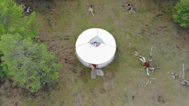 Cinematic aerial drone view of a single Mongolian yurt ger near forest edge in northern Mongolia. Isolated ger dwelling surrounded by woodland and grassland, capturing traditional nomad life and seren