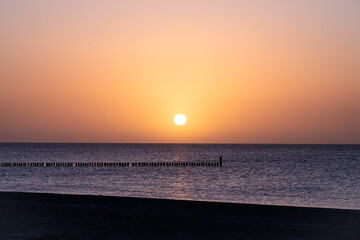 Obraz premium A peaceful sunrise at the sea with warm, vibrant colors and a tranquil horizon; wooden groyne for coastal protection on the south beach of 23775 Großenbrode, Baltic Sea, Germany