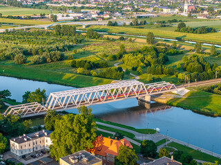 Nowoczesny most kolejowy nad rzeką Odrą w Opolu, widok z lotu ptaka. Panorama miasta z zielonymi terenami nadbrzeżnymi w świetle zachodzącego słońca. Polska infrastruktura. © Henryk Niestrój