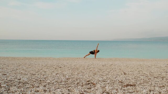Woman practicing yoga pose on peaceful pebble beach beside calm turquoise sea water