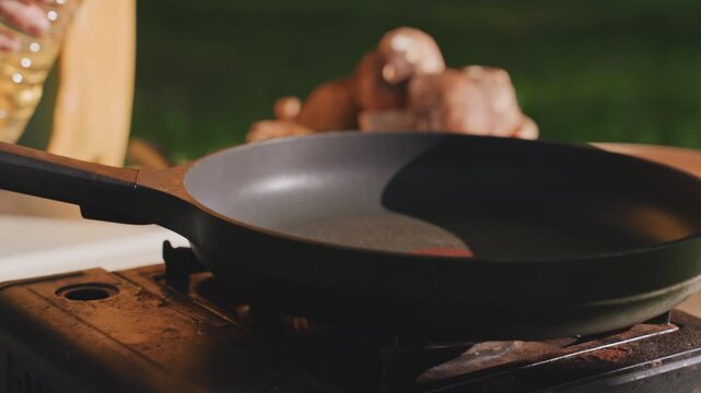 Close up camping pan oil pour hands adding oil to skillet near mushrooms and red camping chair, tranquil morning light, outdoor prep by white camper, rustic campsite table and portable stove