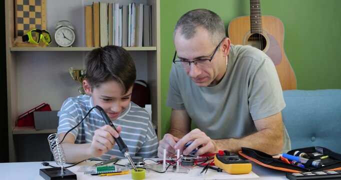 Father and son engage in electronics project. They use tools to create device together. Scene reflects bonding through technology. Learning and discovery occur during this creative process Happy child