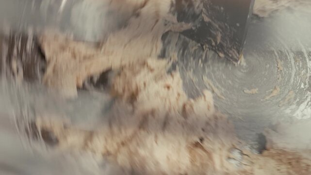 Mixing dough in a stainless steel bowl with a metal spatula, showing the continuous blending process of ingredients in a kitchen setting