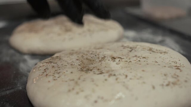 Dough preparation process with seasoned bread dough being shaped and placed on a floured surface in a kitchen setting, showcasing the culinary art of baking