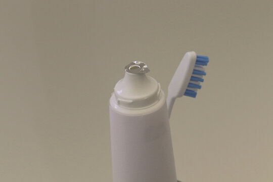 Nahaufnahme einer vom Deckel befreiten Zahnpastatube mit Fokus des Blicks auf das noch anhaftende Aluminiumsiegel sowie fabrikneuer Zahnb&uuml;rste im Hintergrund.