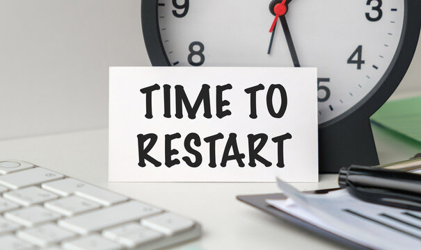 Time To Restart text on a white card standing on an office desk with a clock and keyboard, symbolizing fresh starts and business recovery.