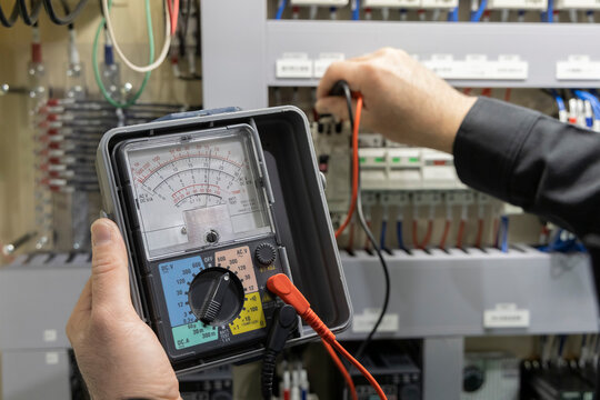 電気設備点検でアナログテスターを使い電圧を測定する電気工事士の手元 制御盤のメンテナンス風景