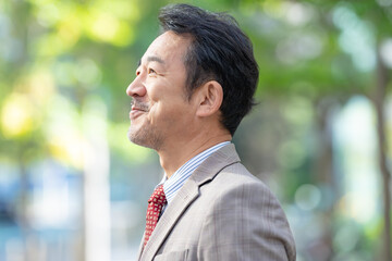 新緑に立つスーツを着たミドル男性ビジネスマン