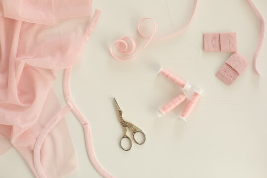 Flat lay composition with scissors and sewing supplies on the table. Crafting essentials for sewing projects with fabric, threads, and tools, ribbon tapes on white background.