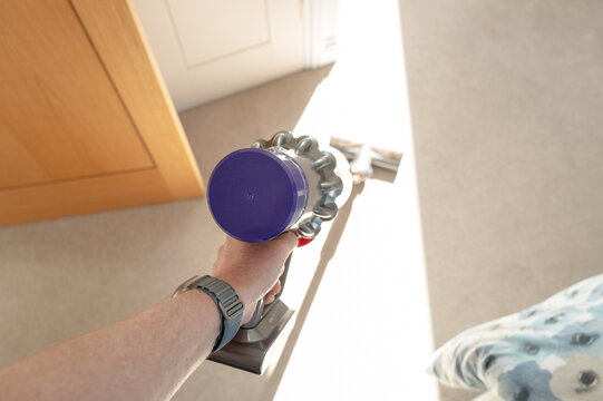Homeowner seen using a popular cordless vacuum cleaner in a bedroom during a sunny morning. Part of the duvet can be seen.