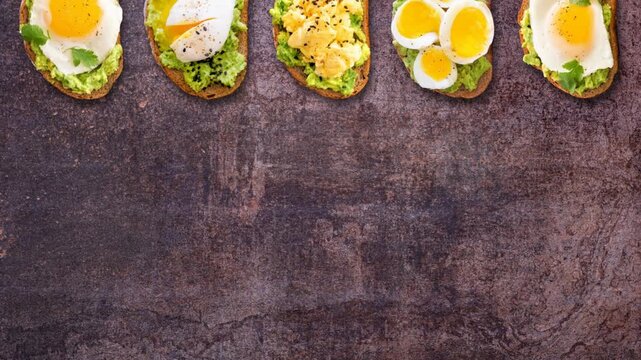 Assortment of avocado egg toasts on sourdough bread. Moving top border. Stop motion loop video on a dark stone background. Fried, poached, scrambled and boiled.
