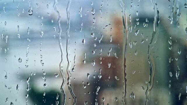 Raindrops on window glass with blurred city background, raindrops sliding down a window pane, raindrops on window glass.