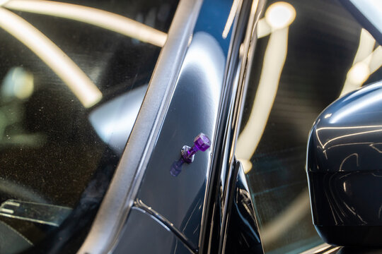 Violet plastic sticker with glue to make dent removal procedure at car after hail. Process of paintless dent repair on car body. The mechanic at the auto shop with tools to repair dents in car body. 