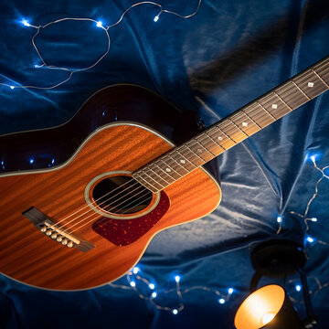 Acoustic guitar on blue fabric with string lights and lamp