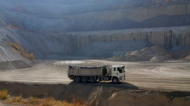 Tracking shot of dump truck hauling material across open pit quarry floor with lateral pan and slow motion dust trails during daytime excavation