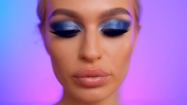 Slow dolly in closeup of woman model posing with shimmering blue eye makeup against purple gradient studio backdrop