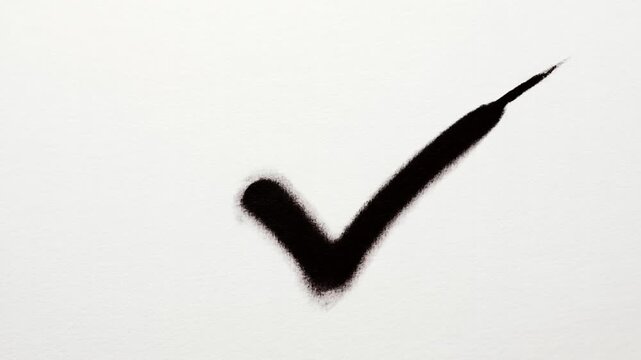 Slow tracking close up shot of marker drawing black check mark across white textured paper in studio setting