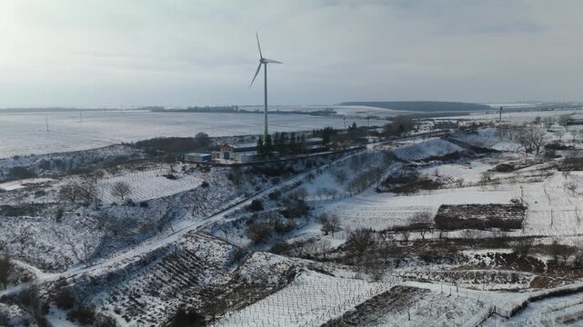 Snow-covered rural landscape with wind turbine, farm buildings, and fields visible in a serene winter setting, showcasing the beauty of nature and agriculture in harmony
