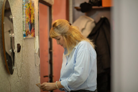 Middle aged woman in blue shirt reading note at home. Mature lady looking at small piece of paper in hallway. Residential interior scene depicting lifestyle of fifty seven year old person.