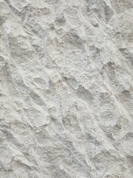 Background of rough ivory white limestone wall texture with diagonal carved lines, up close. Uneven natural stone surface with abstract strokes and diagonal carved lines, for architectural design.