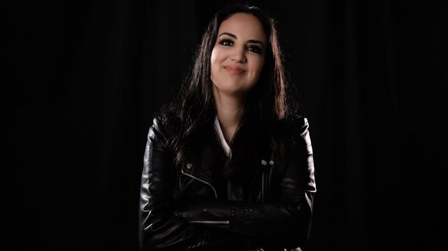 Confidence and self-esteem A woman in a leather jacket smiles against a black backdrop in a studio shot commercials documentaries and editorial projects.