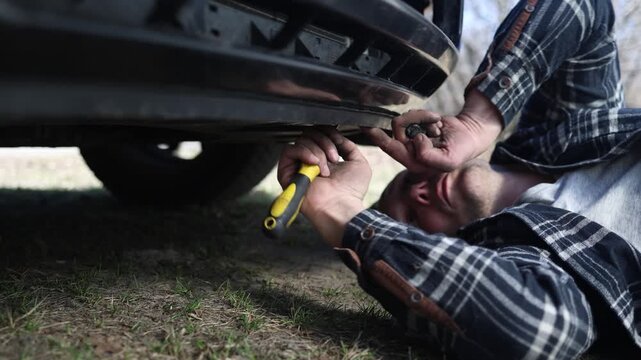 close up of the mechanic's hands, who removes the bumper of the car, he repairs the car.
