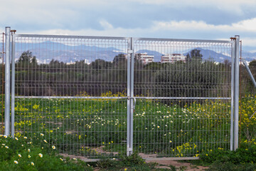 Fototapeta premium Metal fence gate blocking access to green field with city in background
