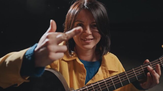 Caucasian woman flipping gesture while camping, strumming acoustic guitar with mischievous smirk and bold attitude, night setting, candid closeup capturing cheeky rebellious humor and raw expression