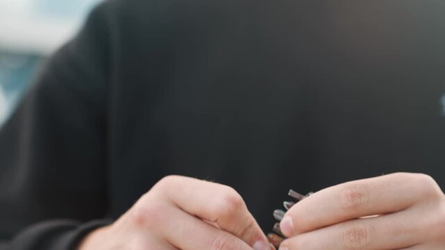 Closeup hands holding single bit white person in urban setting, engineer apprentice studying tiny component, careful thumb and finger grip, reflective sunlight and soft bokeh, methodical examination