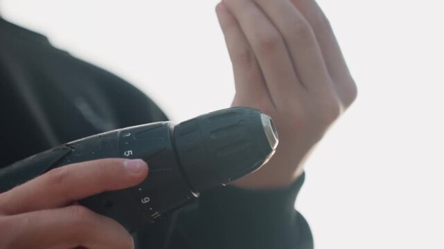 Silhouette of hands controlling drill meticulously. Backlit scene of fingers adjusting drill with precision. Concentrated workshop environment with detailed grip and controlled trigger actions