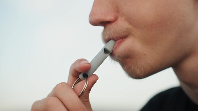 Closeup caucasian student vaping outdoors, profile view of young man using portable mouthpiece on keychain, short stubble, metal device held between fingers, calm reflective mood, soft evening light,