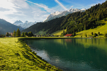 Sunlit Alpine Pasture and Red Barn by a Clear Mountain Lake in Engelberg  © hong