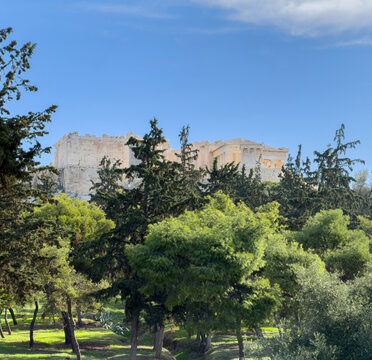 Acropolis propylaea gate ruins above lush trees in Athens, Greece, view from Philopappos Hill, blue sky, sunny day.
