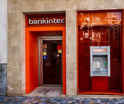The Bankinter branch in Cartagena, Spain, featuring an orange-framed entrance and an ATM set into a window reflecting historic city architecture.
