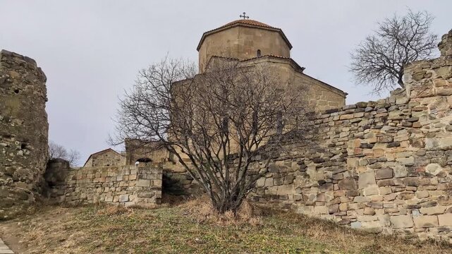 Ancient georgian orthodox jvari monastery of mtskheta with stone walls and a barren tree during a cloudy day, showcasing medieval religious architecture and heritage