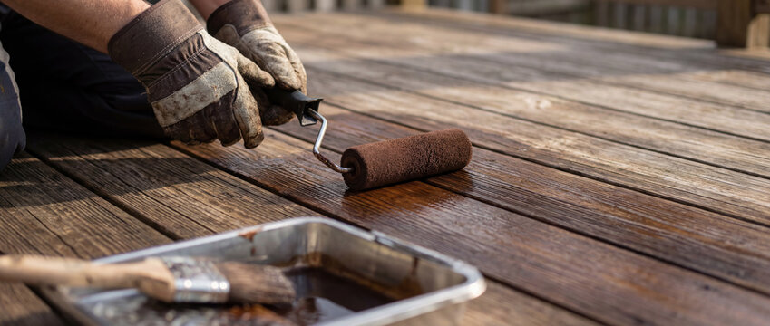 Person staining wooden deck with a paint roller