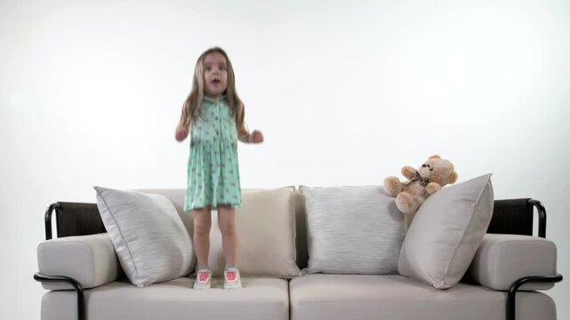 Cute, playful baby is having fun and bouncing on the couch with a soft toy.