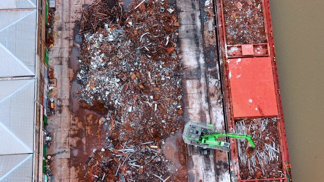 Top down view of recycled metal piles at port terminal. Aerial shot of various scrap metal textures on ground next to cargo ship and green crane.