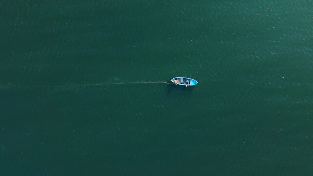 Top view of small blue fishing boat on water. Minimalist aerial shot of a single rowboat on dark green water surface.