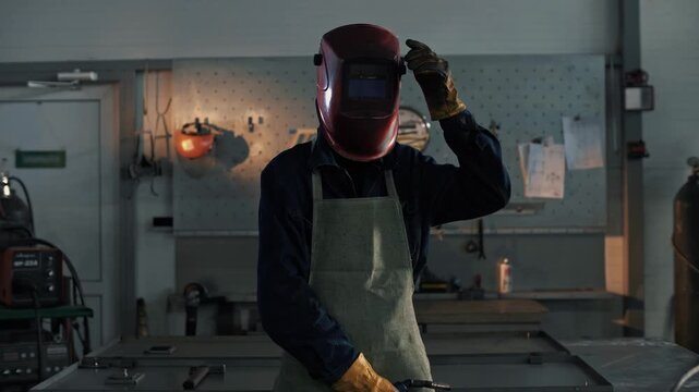 Professional welder looks into the camera and covers the face shield before starting welding work 