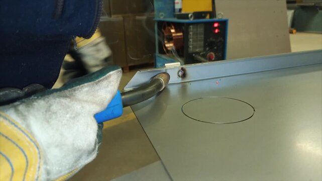 The craftsman is welding a hinge to the cabinet door using gas welding.