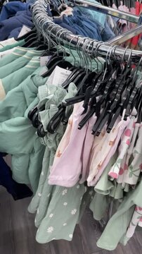 Closeup shopping indoor kidswear rack with neatly arranged hangers, mint and pink patterns visible, tidy retail
