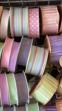 Pastel ribbon spools on shelf, craft browsing indoor shopping aisle soft satin rolls, striped patterns, mint pink lavender hues,