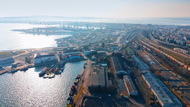 High angle view of industrial port facility and railway. Aerial perspective of warehouses, railway lines, and ship loading zones in a coastal city.