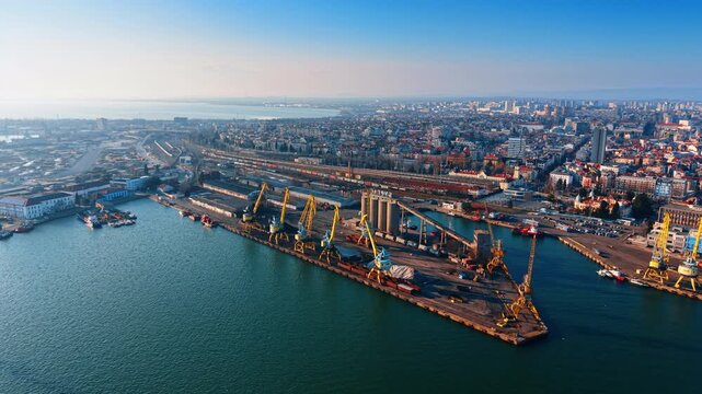 Industrial port terminal with grain elevators and harbor cranes. Panoramic view of a maritime terminal featuring large silos, cranes, and city background.